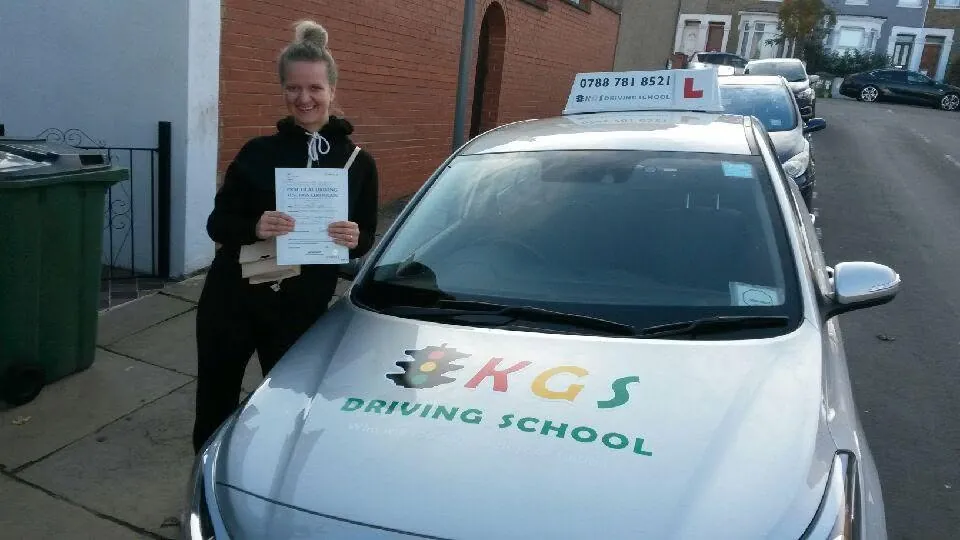 Smiling pupil with her pass certificate next to the KGS Driving School car