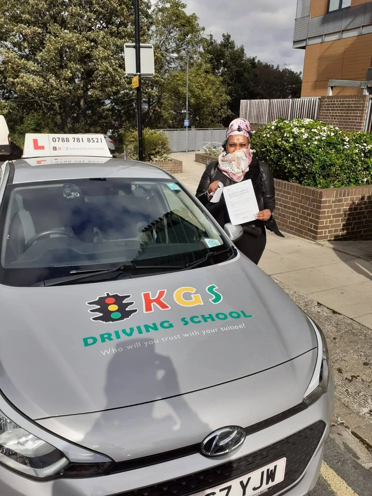 Pupil holding her pass certificate beside the KGS Driving School car she took her driving test in
