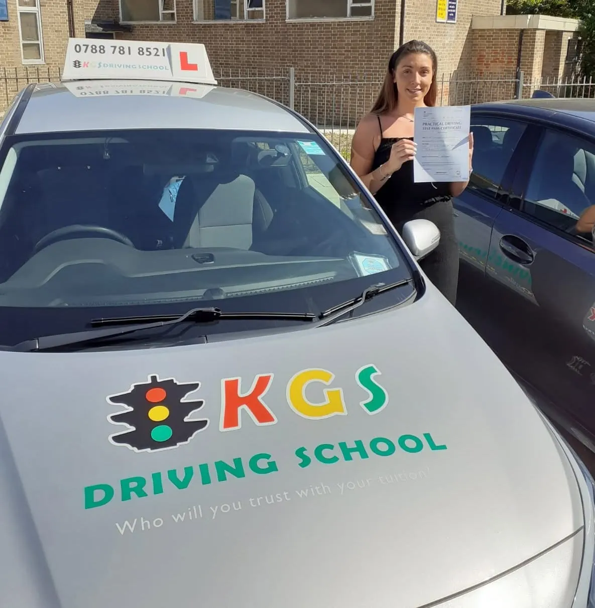 Pupil holding her driving test pass certificate beside the KGS Driving School car