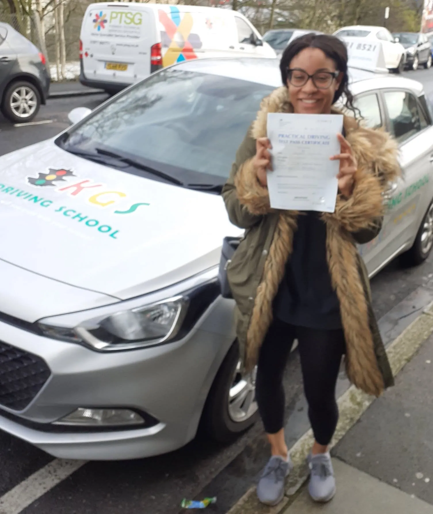 Pupil holding her pass certificate beside the KGS Driving School car